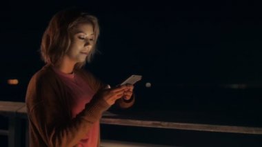 Adorable young woman laughing chatting using smartphone outdoors at night city lights background