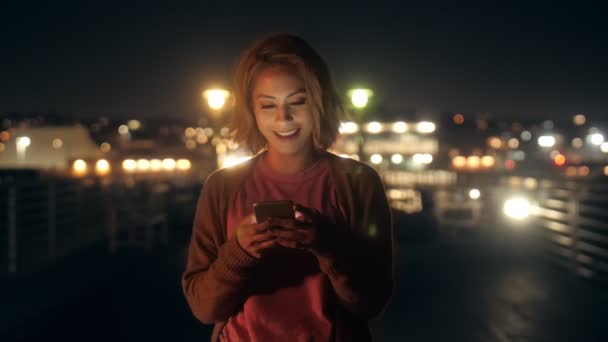 Portrait of happy casual young millenial woman chatting use smartphone on balcony at night — Stock Video