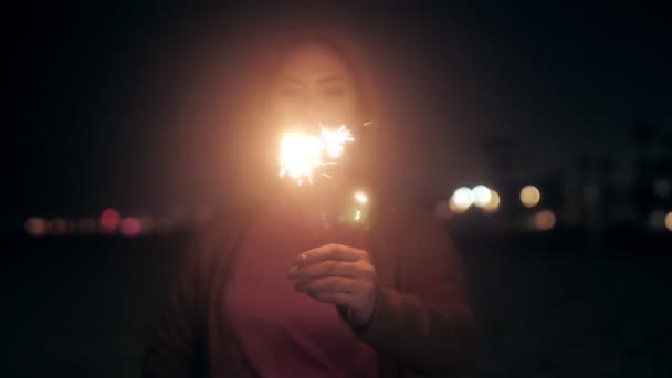 Pleasant millenial woman posing with sparklers at night beach medium close up — Stockvideo