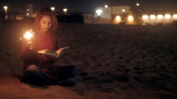 ผู้หญิงสาวผ่อนคลายอ่านหนังสือที่มีแสงสว่างส่องสว่างที่ชายหาดกลางคืนมีอารมณ์บวก — วีดีโอสต็อก