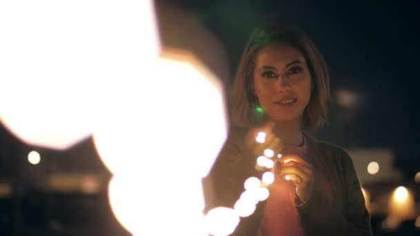 Happy pleasant young millenial girl playing lights garland at night outdoors having fun — Wideo stockowe