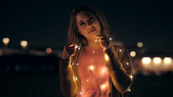 Portrait of smiling casual millenial woman posing outdoors holding lights garland — ストック動画