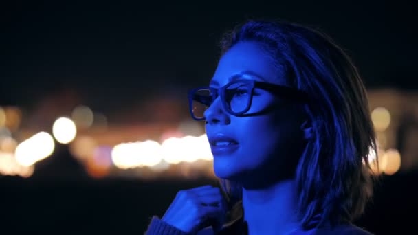 Close up face of millenial woman in glasses looking on blue neon shining at outdoors night party — ストック動画