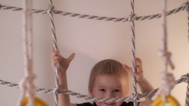 Close up happy little cute boy climbing on rope ladder having fun at home