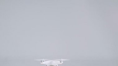 Active small white unmanned quadrocopter drone with action camera flying rising up at studio