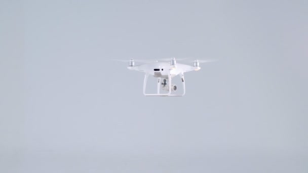 Active small white unmanned quadrocopter drone with action camera flying turning around at studio — Stock Video