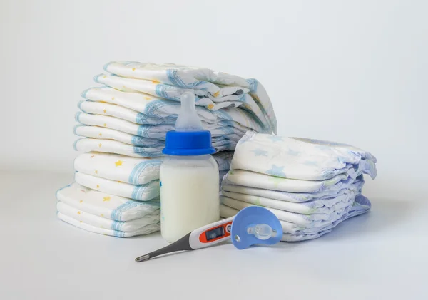 Pilha de fraldas descartáveis para bebês, chupeta e termômetros eletrônicos sobre fundo branco . — Fotografia de Stock