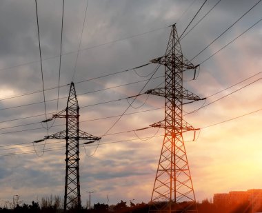 Yüksek gerilim elektrik direği silüeti. Günbatımı gökyüzü arka plan.