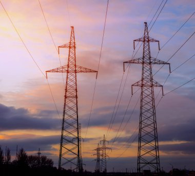 Yüksek gerilim elektrik direği silüeti. Günbatımı gökyüzü arka plan.