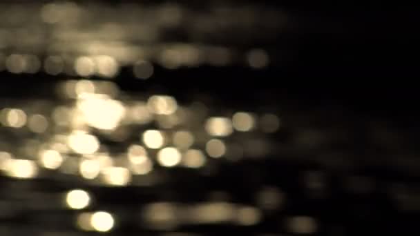Goldene Bokeh-Reflexe auf dem Wasser vor dunklem Hintergrund — Stockvideo