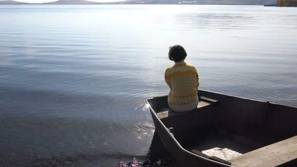 Junge brünette Mädchen sitzt in einem Boot auf dem See. Hintergrund Sonneneinstrahlung auf dem Wasser. — Stockvideo