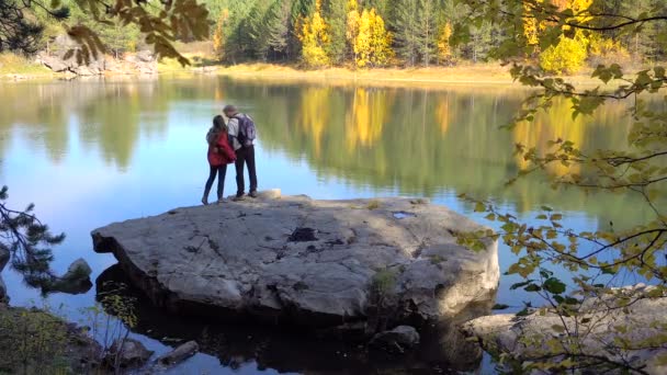 Mladí turisté pár milenců na lesní jezírko. Podzimní listí na podzim slunečný den. Vody na pozadí žluté stromy. — Stock video