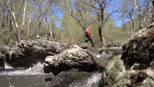 Der junge Mann springt in Zeitlupe über einen Waldbach. Vorfrühling ist ein sonniger Tag, ein großer Wasserstrom. — Stockvideo