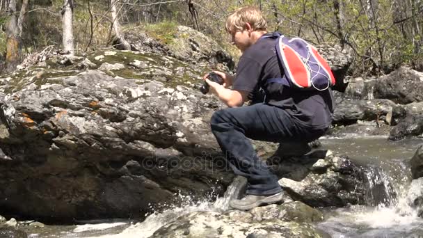 Jovem Loira Fotografa Fluxo Florestal. Início da primavera é um dia ensolarado, uma grande corrente de água . — Vídeo de Stock