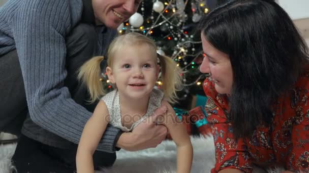 Familia joven acostada en una alfombra bajo el árbol de Navidad — Vídeos de Stock