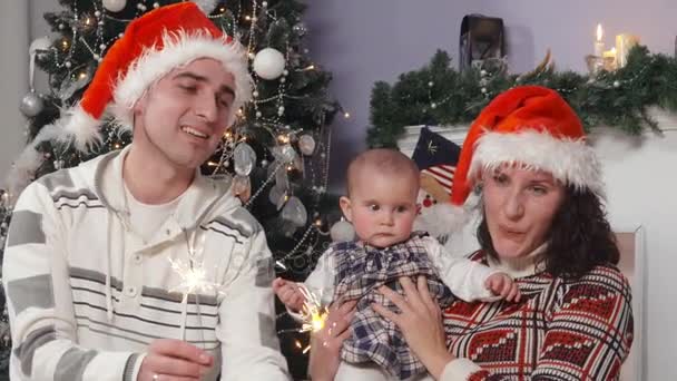 Heureuse famille avec bébé en chapeaux Santas bénéficie de lumières bengales — Video