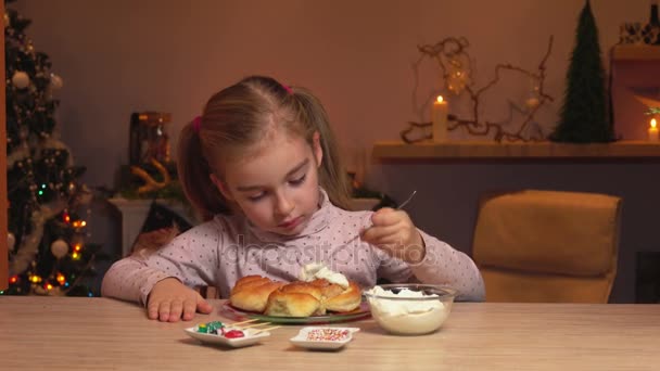 Meisje uitstrijkjes crème op kaneel rollen — Stockvideo