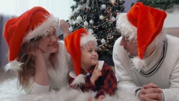 Gelukkige familie in Santas hoeden liggend op het tapijt — Stockvideo