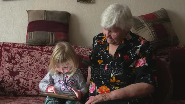 Бабушка с внучкой, смотрящей фотографии на планшете — стоковое видео