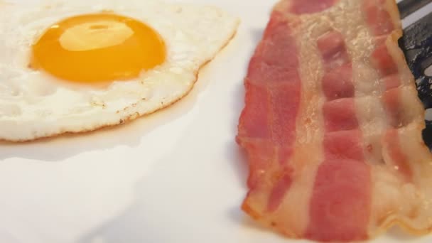 Кладет бекон на белую тарелку с яйцами — стоковое видео