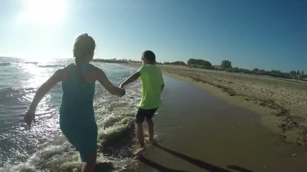 Chica y niño corren en el agua a lo largo de la línea de surf — Vídeos de Stock