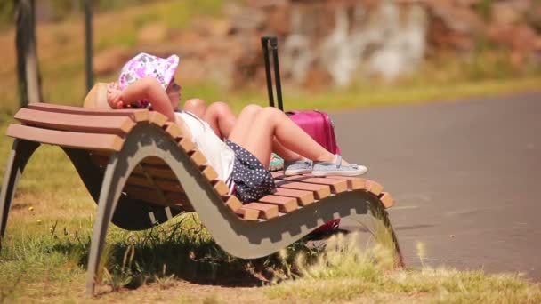 Menino e menina descansando em um banco com uma mala — Vídeo de Stock