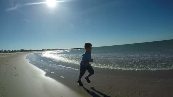 Niño en camiseta azul corre a lo largo de la playa — Vídeo de stock