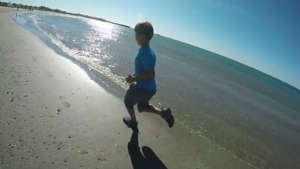 Niño en camiseta azul corre a lo largo de la playa — Vídeo de stock