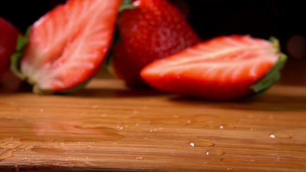 Fresas maduras cayendo sobre un tablero de madera mojado — Vídeos de Stock