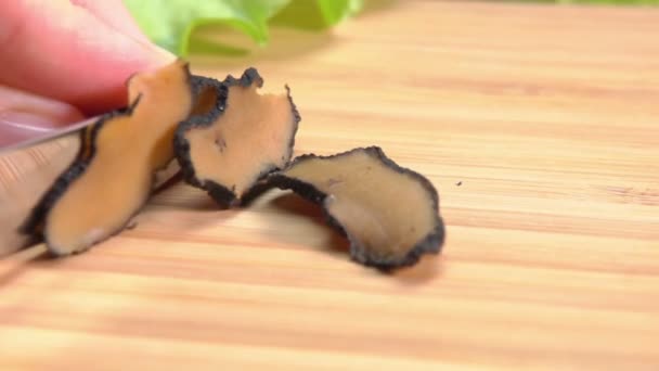 The cook gently cuts the truffle tuber into slices on the wooden board — Stock Video