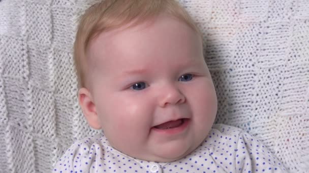 Joyeux bébé aux yeux bleus couché sur la couverture et rit — Video