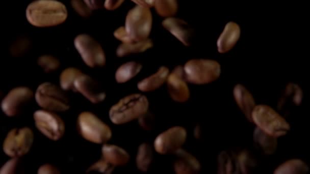 Los granos de café fritos vuelan a la cámara sobre un fondo negro — Vídeo de stock