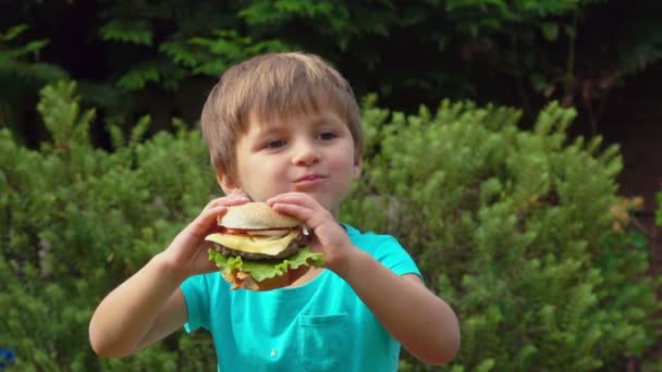 Pojken äter en stor hamburgare med ost — Stockvideo