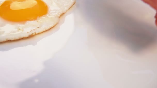 Кладет бекон на белую тарелку с яйцами — стоковое видео