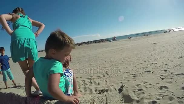 Crianças brincando na praia perto de uma grande pedra — Vídeo de Stock