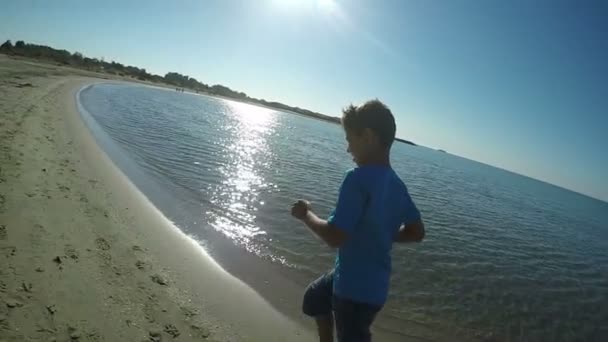 Niño en camiseta azul corre a lo largo de la playa — Vídeos de Stock