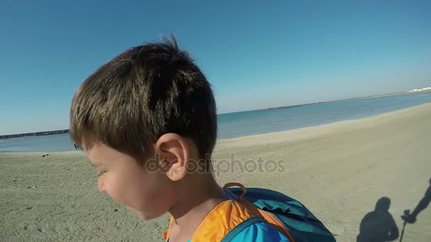 Un niño con una mochila corriendo a lo largo de la orilla del mar — Vídeos de Stock