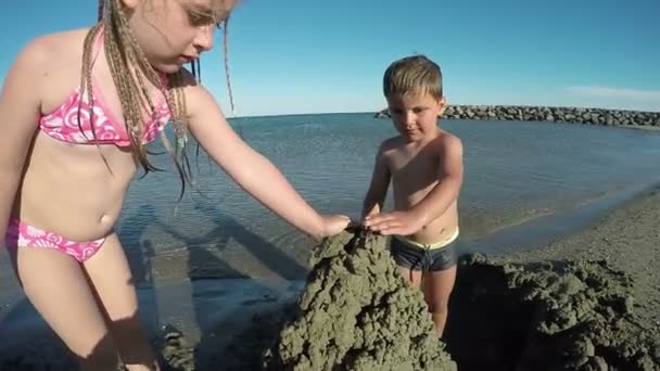 Lilla vackra flicka och pojke bygga slottet sand — Stockvideo