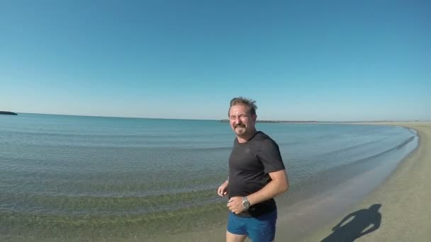 Mannen i en svart T-shirt springer längs stranden — Stockvideo