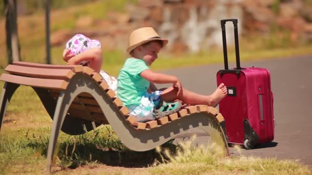 Jongen en meisje rusten op een bankje met een koffer — Stockvideo