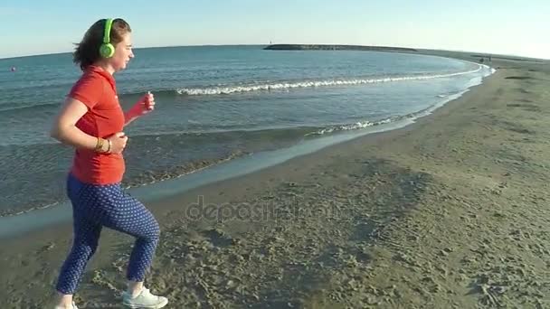 Girl runs along the beach in green headphones — Stock Video