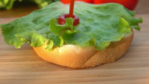 Шеф-повар кладет лист салата на булочку — стоковое видео