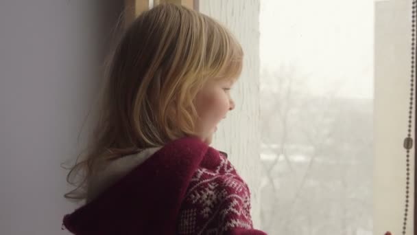 Schöne blauäugige Mädchen blickt durch das Fenster — Stockvideo