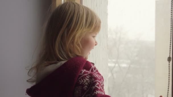 Beautiful blue-eyed girl looks through the window — Stock Video