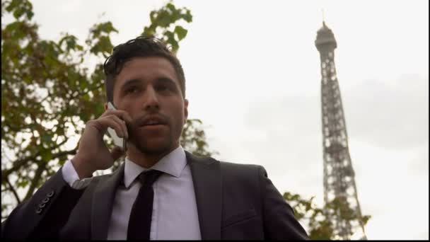 Привабливим чоловіком в костюмі набуває смартфон, поруч із Ейфелевою вежею на selfie — стокове відео
