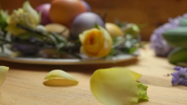 Rosenblätter fallen auf einen Tisch vor einem Hintergrund farbiger Ostereier — Stockvideo
