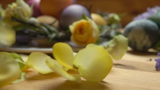 Bloemblaadjes van een gele roos vallen op een tafel tegen een achtergrond van paaseieren — Stockvideo