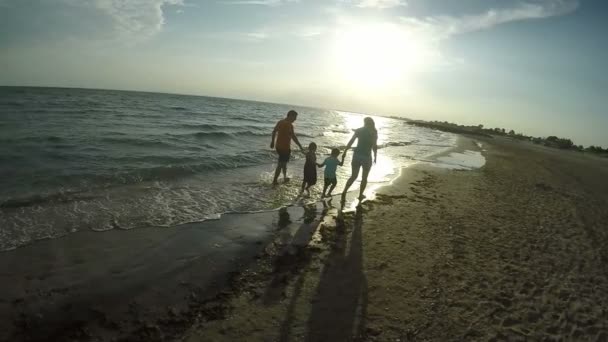 Família caminhando ao longo do mar ao pôr do sol — Vídeo de Stock