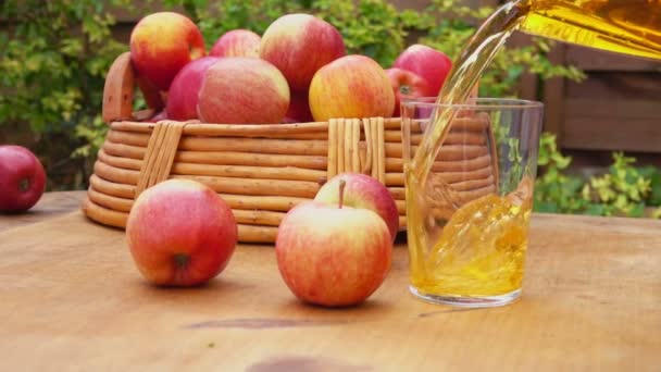 Χυμό μήλου και ένα καλάθι με ώριμα μήλα σε ένα ξύλινο τραπέζι — Αρχείο Βίντεο