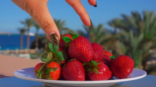 Mano toma una fresa jugosa grande de un plato — Vídeo de stock